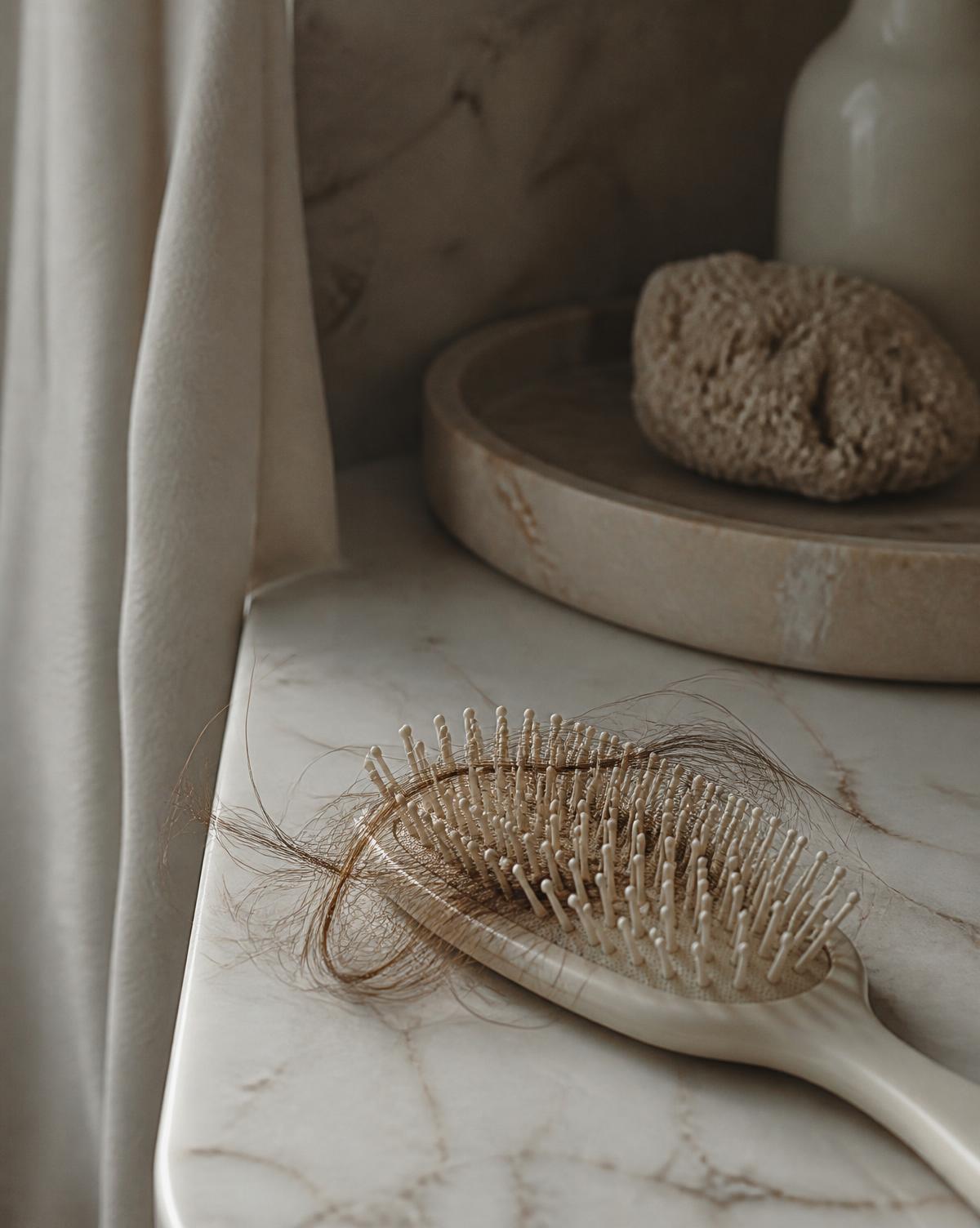 Brosse à cheveux posée sur un plan en marbre, mèches de cheveux prises dans les picots.